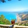 A balcony with a potted plant above a mountainous, seaside landscape